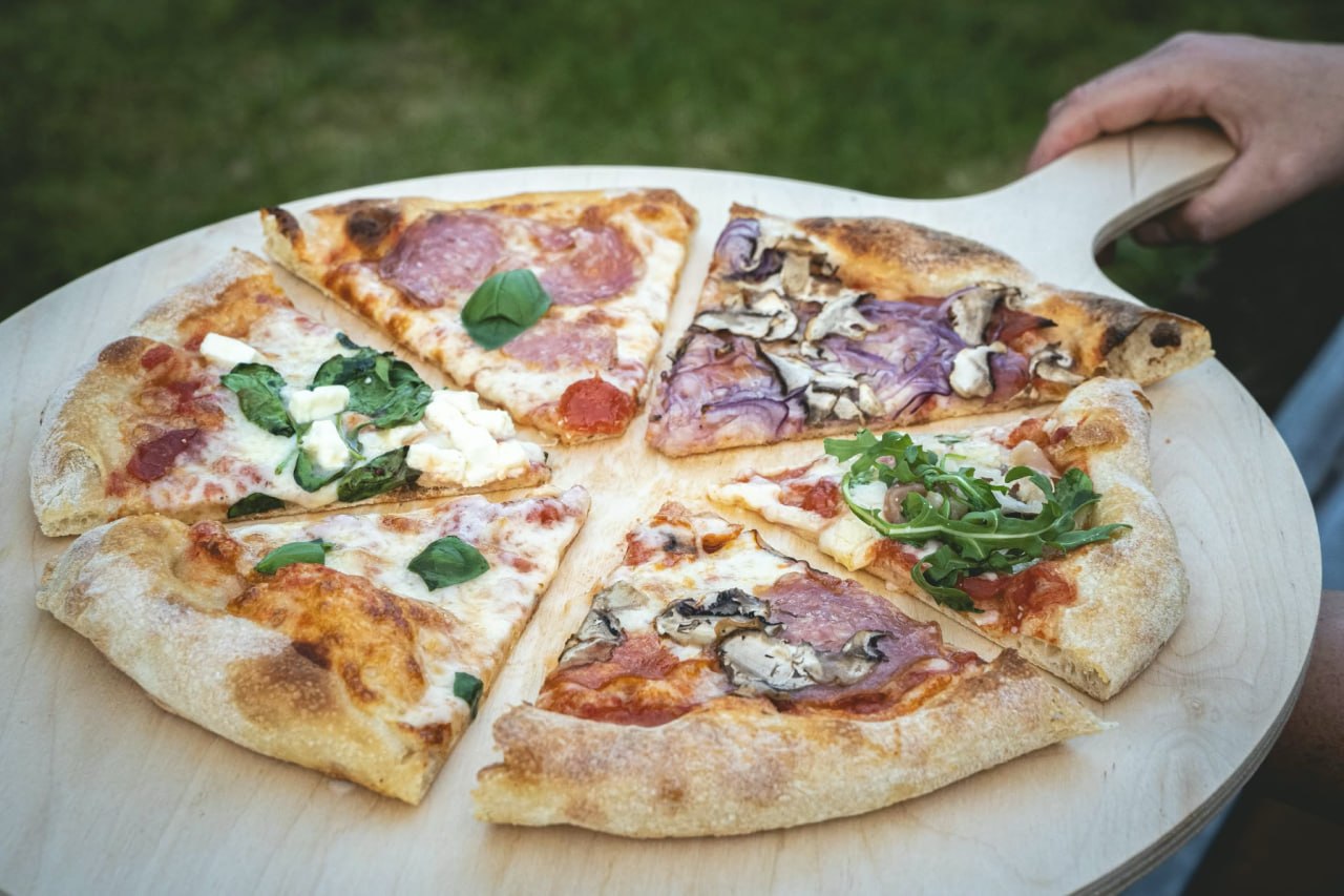Gemischte Pizzascheiben mit verschiedenen Belägen auf Holzplatte im Grünen