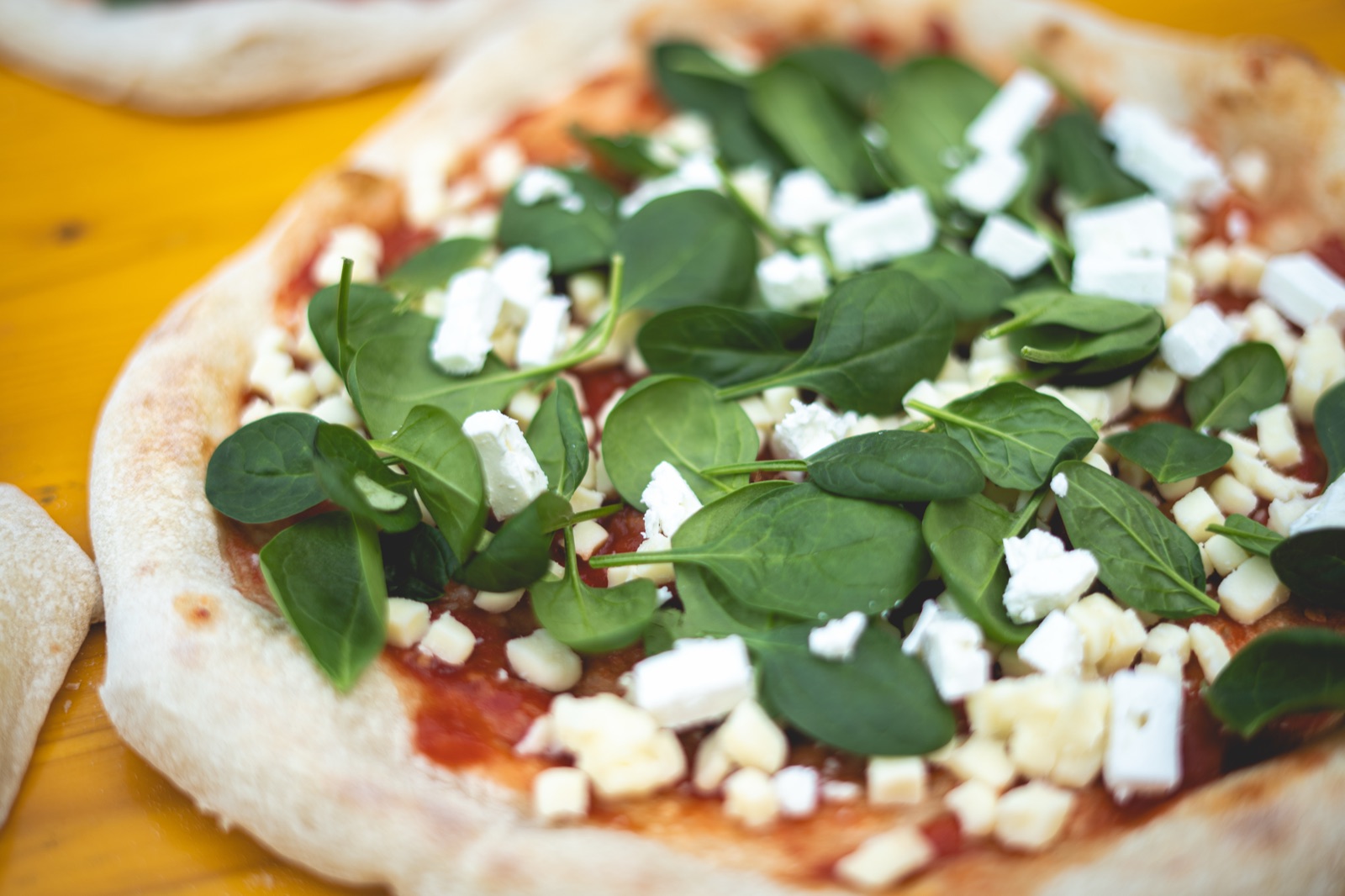 Frische Pizza belegt mit Blattspinat und Feta vor dem Backen